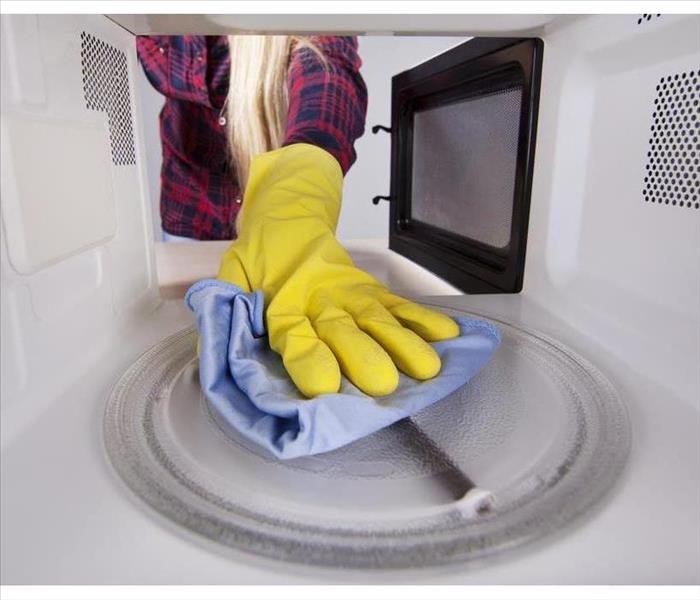 Closeup of hand in protective glove wiping rag in microwave. View from the interior of the oven