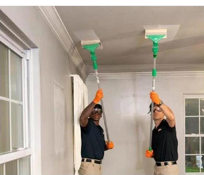 Two technicians cleaning soot damage from a ceiling